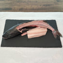Two fish on a black cutting board with packaged products in the background